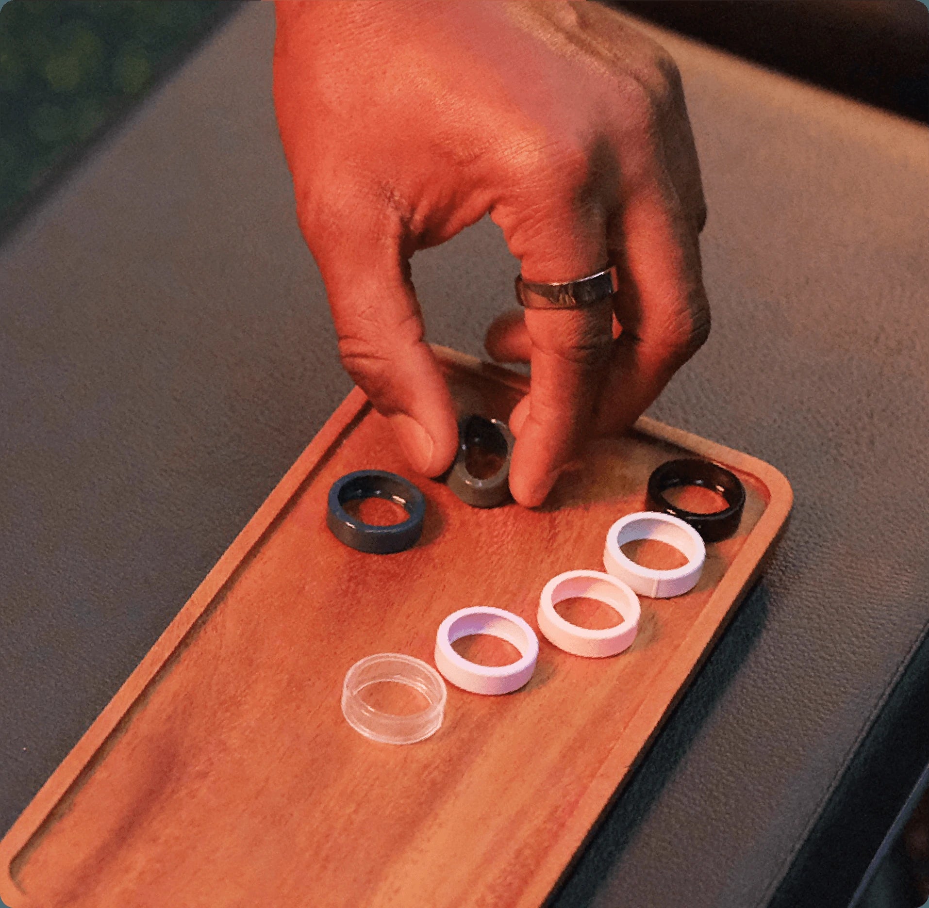 Person's hand arranging smart rings on a wooden tray, showcasing various colors and designs.