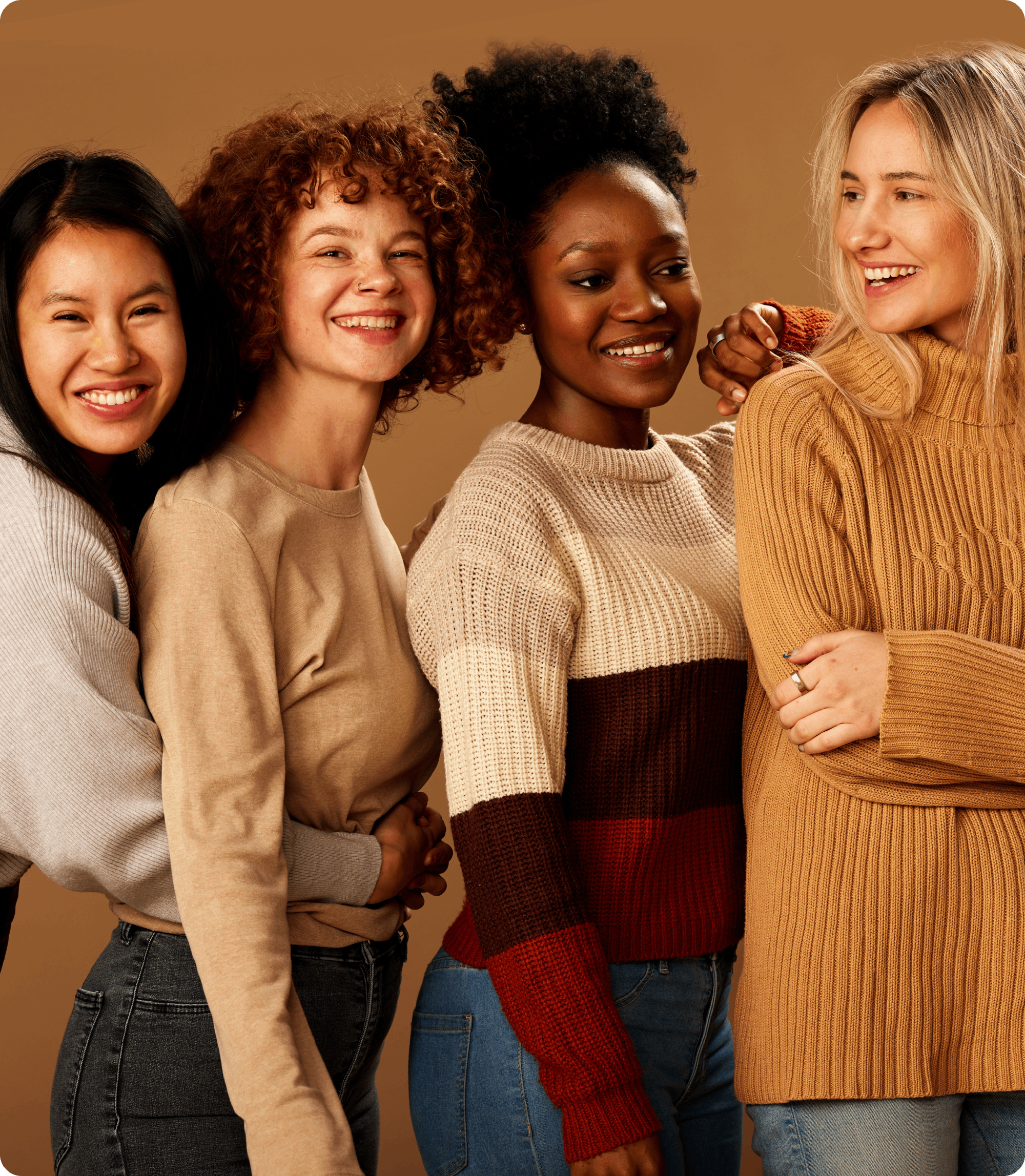 Four women smiling, wearing sweaters and jeans